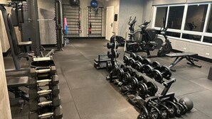 Uma academia com equipamentos de musculação, aparelhos de ginástica e uma grande janela.