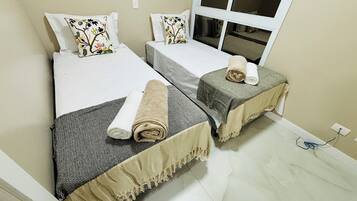 Um quarto com duas camas de solteiro, cada uma com um cobre-leito estampado e uma toalha enrolada.