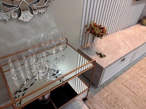 Ein Zimmer mit einem Glastisch, der Weingläser, eine Vase mit Blumen und einen Schlüssel auf der Ablagefläche beherbergt.
