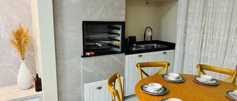 Una cocina moderna con horno empotrado, un lavamanos y un comedor con una mesa de madera dispuesta para cuatro personas.