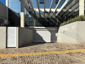 A modern building with a glass facade, a closed roller shutter door, and a tactile paving path. - Ravello Elegance Center Foz do Iguaçu (Foz do Iguaçu)