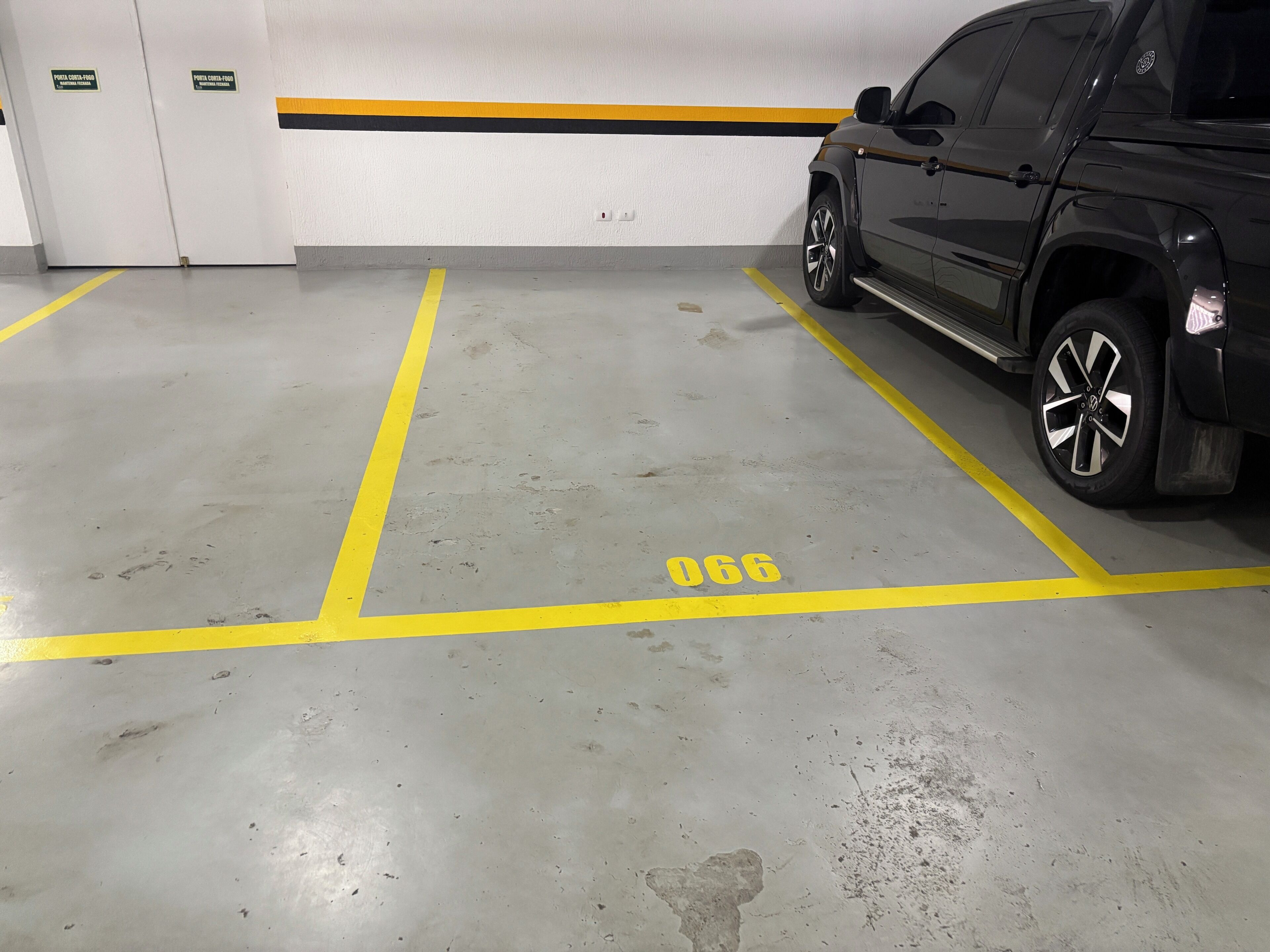 Um estacionamento com um veículo estacionado em uma vaga marcada com o número 066.