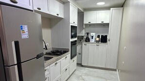 Uma cozinha com geladeira de aço inoxidável, fogão a gás, armários brancos e piso revestido de azulejos.