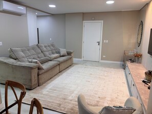 A living room with a beige sofa, a coffee table, a TV, and a door. - Ravello Elegance Center Foz do Iguaçu (Foz do Iguaçu)