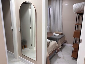 A bedroom with a large mirror, a bed with a headboard, a bedside table, a shelf, and a window with curtains. - Ravello Elegance Center Foz do Iguaçu (Foz do Iguaçu)
