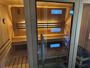 En sauna med træbænke og glasdøre, et håndklædestativ og et lille vindue.