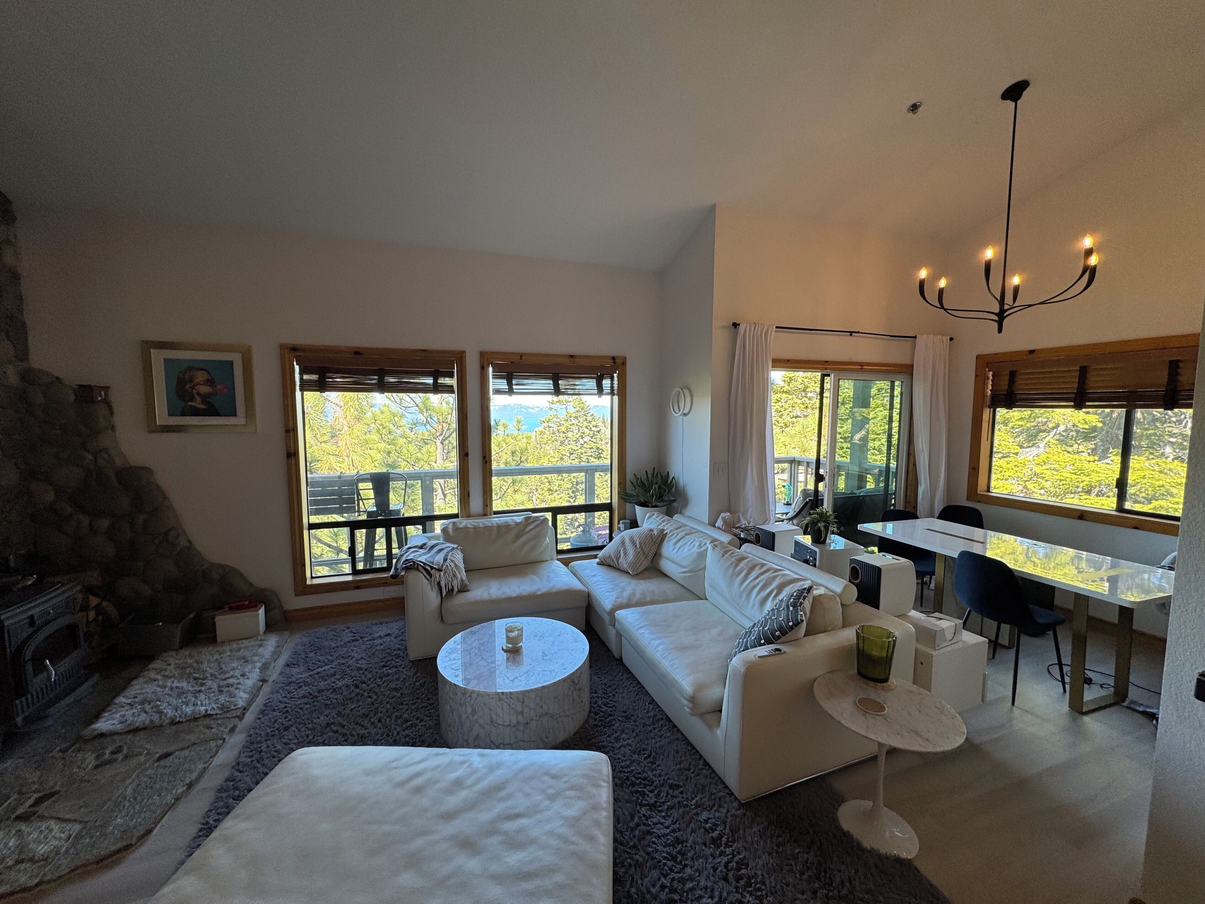 A modern living room with a stone fireplace, large windows, a dining area, and a cozy seating arrangement.