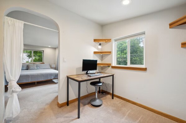 Quarto com cama, escrivaninha com computador, janela e vista para o verde lá fora.