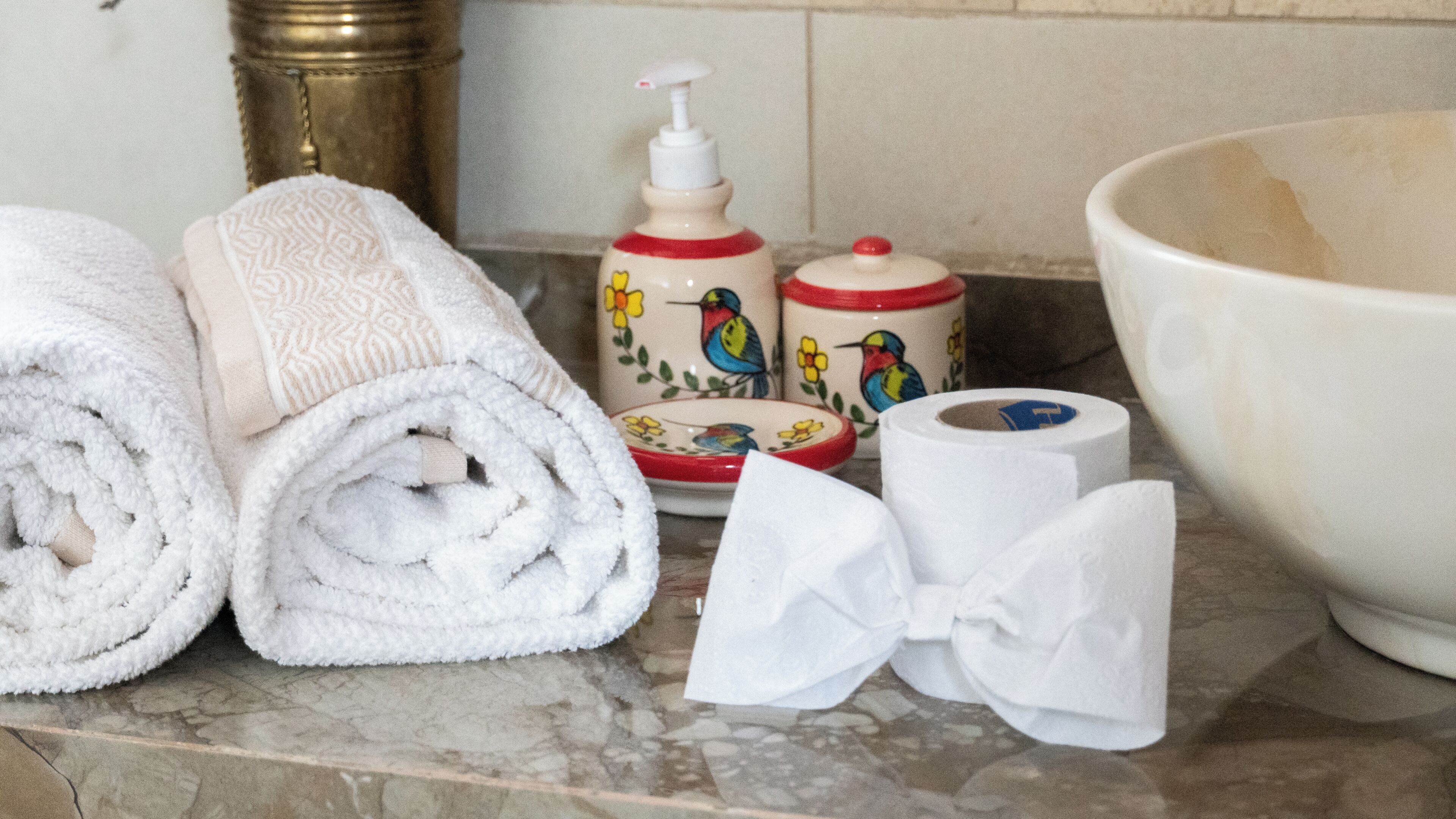 Een badkamermeubel met opgerolde handdoeken, een zeepdispenser, een toiletrol en een grote wasbak.
