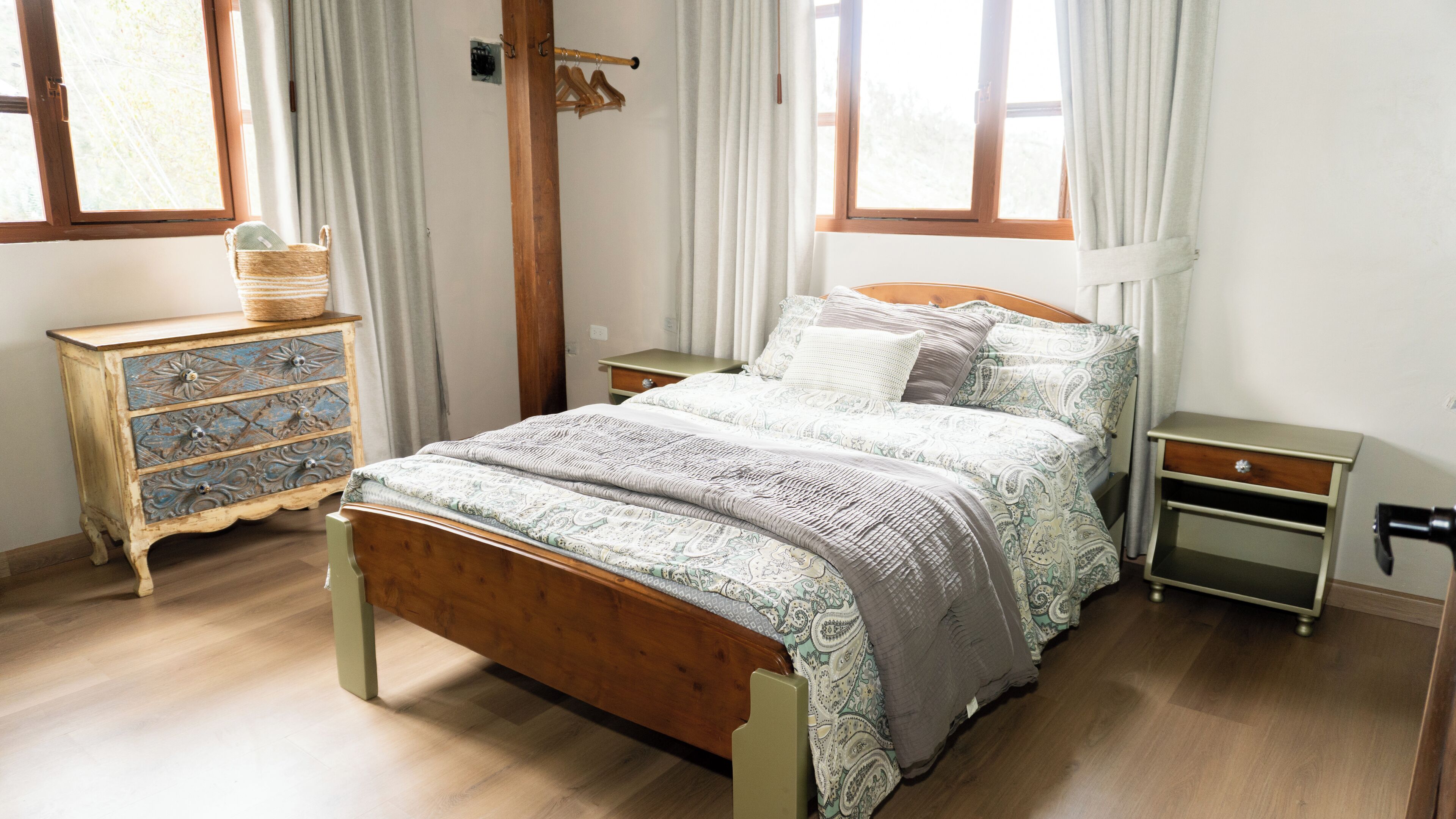 Una camera da letto con un letto di legno, una cassettiera, un comodino e una finestra con tende.