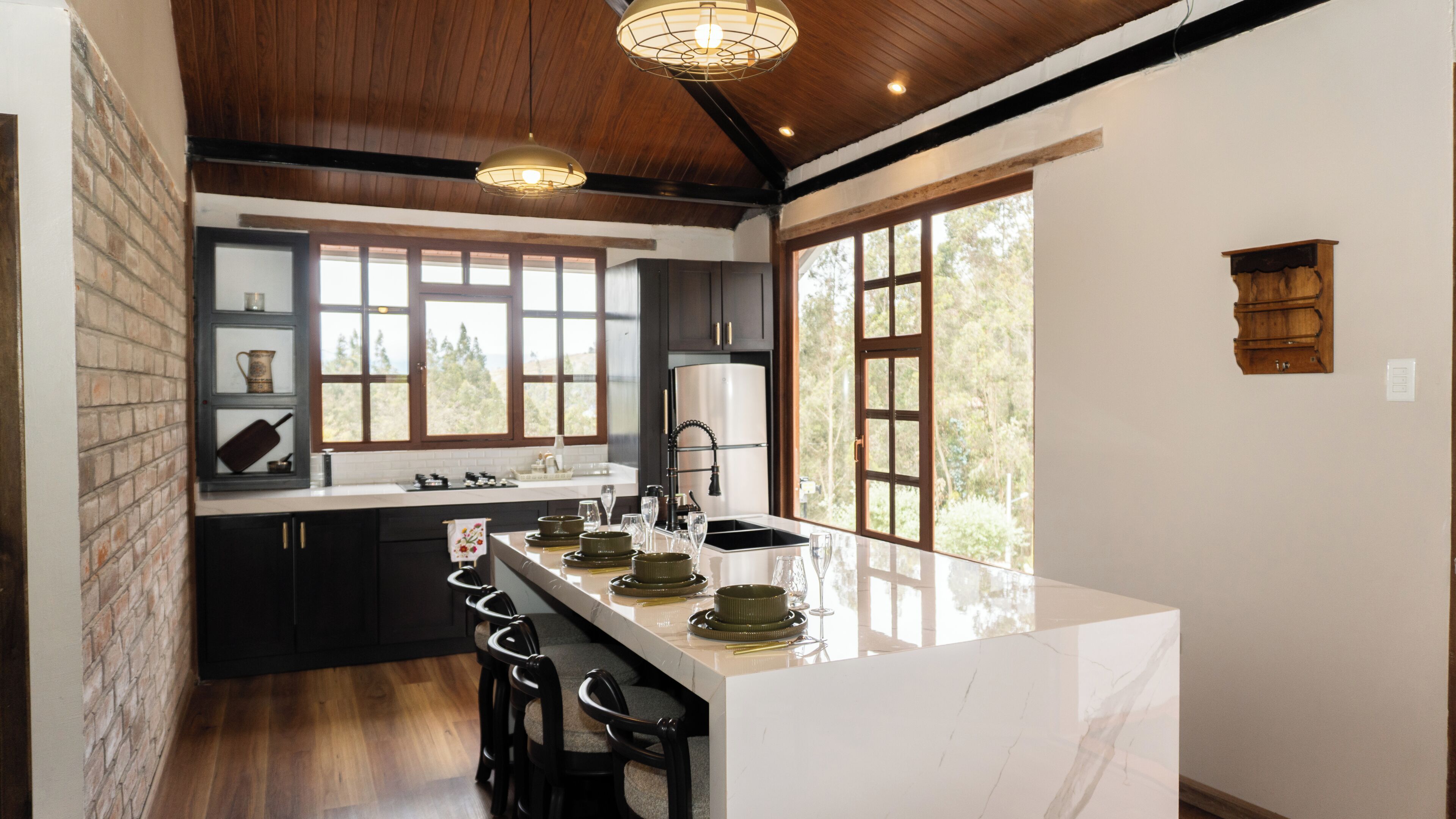 A modern kitchen with a marble island, dark cabinetry, and large windows.