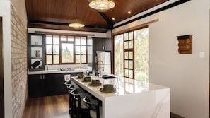 A modern kitchen with a marble island, dark cabinetry, and large windows. - Vacation Home 10 minutes from Ambato, 40 minutes from Baños de Agua Santa (Ambato)