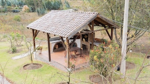 Uma estrutura rústica ao ar livre, com telhado de telhas, forno de tijolos e área de estar.