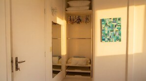 A closet with hanging clothes, a shelf, and a painting on the wall. - Apto Beira-mar com Garagem na Praia da Costa (Vila Velha)