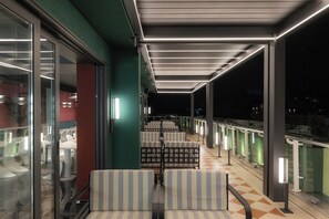 A covered outdoor seating area with striped chairs and tables, a glass railing, and a view of the night sky. - Proza Hotel & Restaurant (Kutaisi)