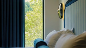 A hotel room with a bed, a window, and a view of trees.