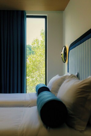 A hotel room with a bed, a window, and a view of trees.