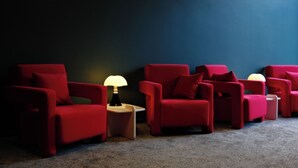 A row of red armchairs with a lamp between them, against a dark wall.