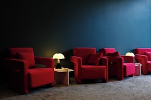 A row of red armchairs with a lamp between them, against a dark wall.