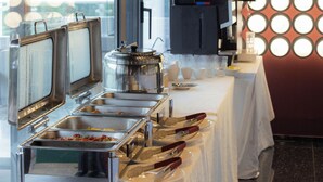 A buffet setup with multiple serving stations, a coffee machine, and a wall with circular light fixtures.