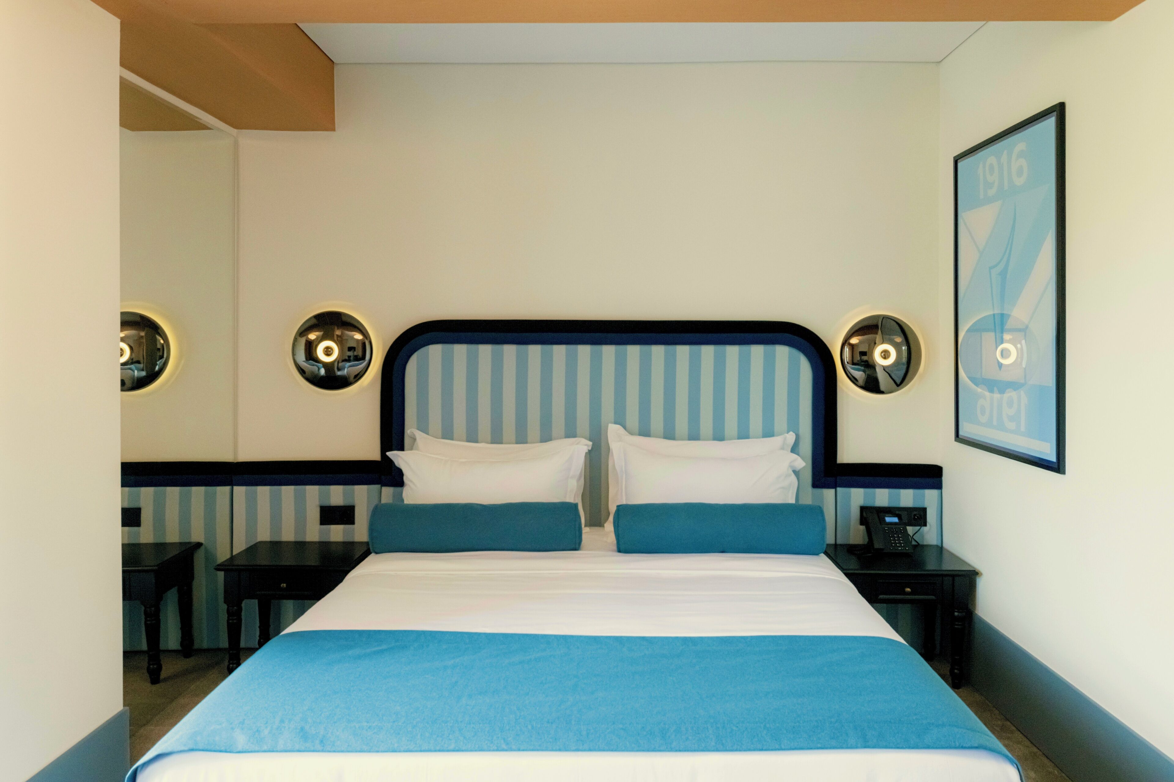 Ein Hotelzimmer mit einem großen Bett, zwei Nachttischen, einem Beistelltischchen mit Telefon und einer Wandleuchte.