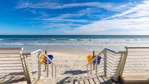 Een strand met een houten looppad en metalen relingen, dat uitkomt op de oceaan.