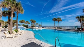 A poolside area with lounge chairs, palm trees, and a clear blue sky. - 2BR Deluxe at WorldMark Ocean Walk on Daytona Beach Near the Boardwalk (Daytona Beach)