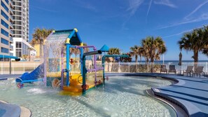 Un parque acuático con tobogán de agua, piscina y zona de playa con sillas de descanso.