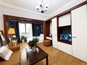 Ein Hotelzimmer mit Bett, Fernseher, Schreibtisch, Stuhl, Lampe und einer Zimmerpflanze.