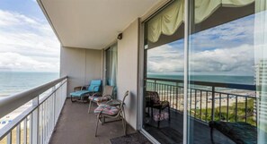 Ein Balkon mit zwei Loungestühlen und einem kleinen Tisch, der auf einen Strand und den Ozean blickt.