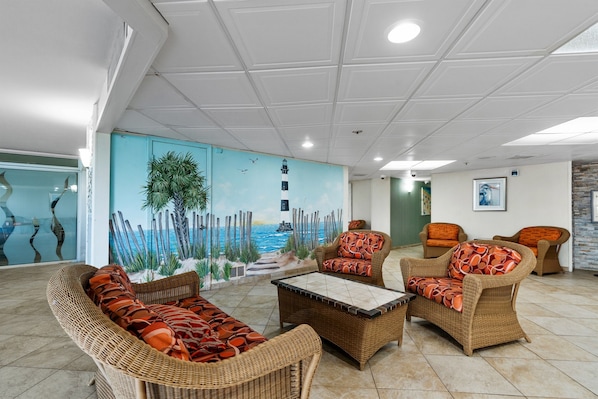 A lounge area with wicker furniture, a mural of a lighthouse, and a view of the sea. - S Hampton 1603 2 Br Oceanview in Kingston, Pool (Myrtle Beach)
