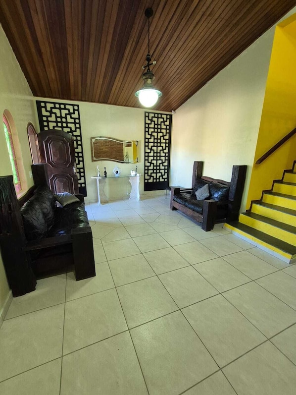A spacious living area with a wooden ceiling, a black leather sofa, a white coffee table, and a staircase with yellow steps.