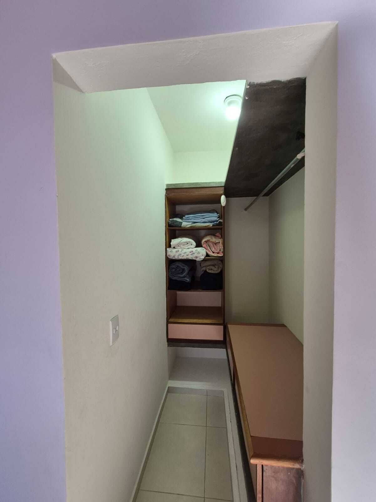 A narrow hallway with a wooden closet containing folded clothes and a shelf.