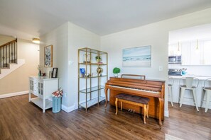Ein Wohnzimmer mit einem Klavier, einem weißen Schrank, einer Glastrennwand und einem Bild an der Wand.