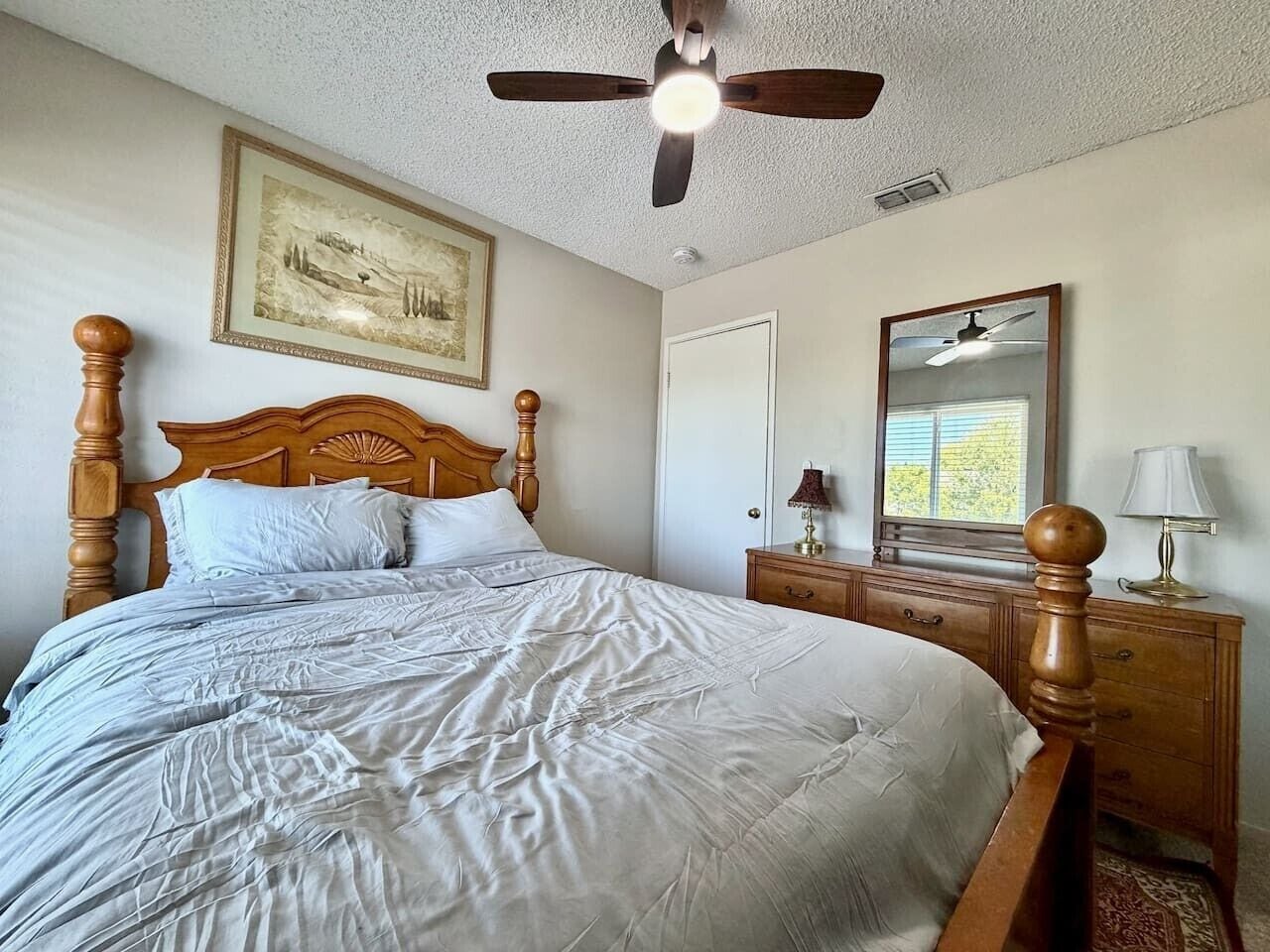 A bedroom with a bed, a dresser, a mirror, and a ceiling fan.