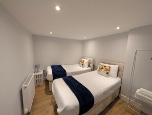 Ein Hotelzimmer mit zwei Betten, einem Heizkörper, einem Schreibtisch mit Lampe und einem Handtuchhalter.