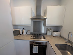 Eine kleine Küche mit Gaskochfeld, Backofen, weißen Schränken und einer Edelstahl-Dunstabzugshaube.