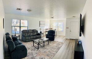 A spacious living room with a sectional sofa, a recliner, a coffee table, and a flat-screen TV mounted on the wall. - Prime North Scottsdale Retreat Near Golf, Hiking, Shops, Dining & Loop 101 (Scottsdale)