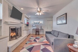 A living room with a fireplace, a ceiling fan, a sofa, a desk, and a patterned rug. - Your Home Away From Home, Charming 1-bedroom apartment with everything you need. (Riverton)