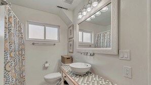 Un baño con un lavamanos blanco, un espejo con iluminación, un inodoro y una cortina de ducha con estampado floral.