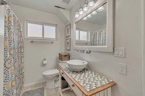 Ein Badezimmer mit weißem Waschbecken, einem beleuchteten Spiegel, einer Toilette und einer Duschvorhang mit floralem Muster.