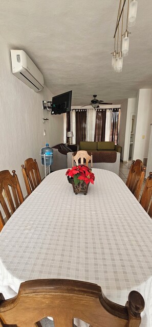 A dining area with a round table, chairs, a television mounted on the wall, and a ceiling fan. - Casa Bonita in Nuevo Vallarta: Enjoy Your Beach Vacation (Mezcales)