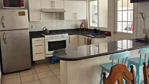 A kitchen with white cabinets, a stove, a microwave, and a refrigerator. There is a dining table with chairs. - Casa Bonita in Nuevo Vallarta: Enjoy Your Beach Vacation (Mezcales)