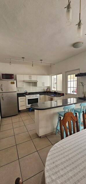 A kitchen with white cabinets, a stove, a microwave, and a refrigerator. There is a dining table with chairs. - Casa Bonita in Nuevo Vallarta: Enjoy Your Beach Vacation (Mezcales)