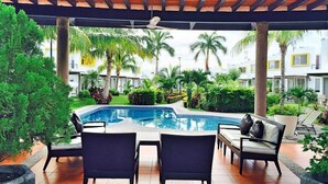 A pool area with a covered patio, lounge chairs, and a view of the surrounding greenery and buildings. - Casa Bonita in Nuevo Vallarta: Enjoy Your Beach Vacation (Mezcales)