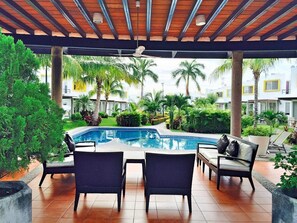 A pool area with a covered patio, lounge chairs, and a view of the surrounding greenery and buildings. - Casa Bonita in Nuevo Vallarta: Enjoy Your Beach Vacation (Mezcales)