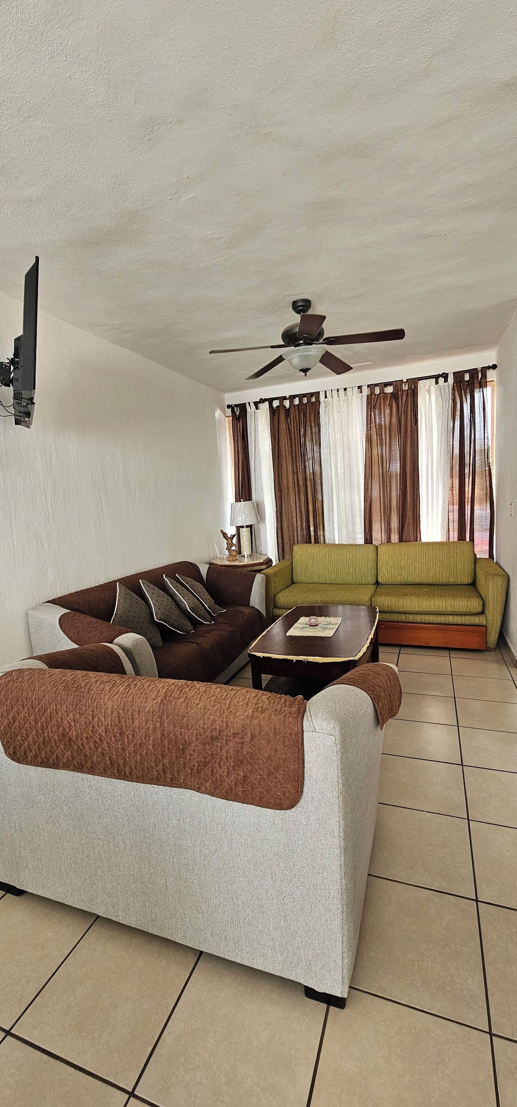 A living room with a sofa, a coffee table, a ceiling fan, and a window with curtains.