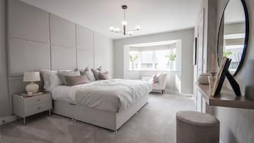 A modern bedroom with a large bed, bedside tables, a nightstand, a mirror, and a window with natural light.