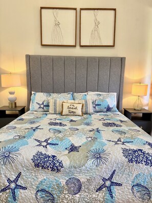 Un lit recouvert d’une couvre-lit aux motifs bleus et blancs évoquant l’océan, deux œuvres d’art encadrées accrochées au mur et deux lampes de chevet.