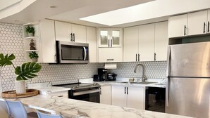 A modern kitchen with a central island, bar stools, a stainless steel refrigerator, and a microwave. - Family Retreat @Palm 5 Golf View (Palmas del Mar)